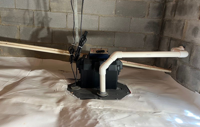 Sump pump installed on a vapor barrier in a crawlspace, with PVC discharge pipe routed along a concrete block foundation wall