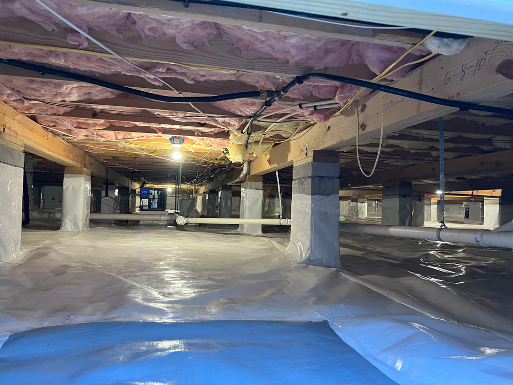 Spacious crawlspace with a vapor barrier installed on the ground, exposed pink fiberglass insulation above, and concrete piers supporting the floor structure