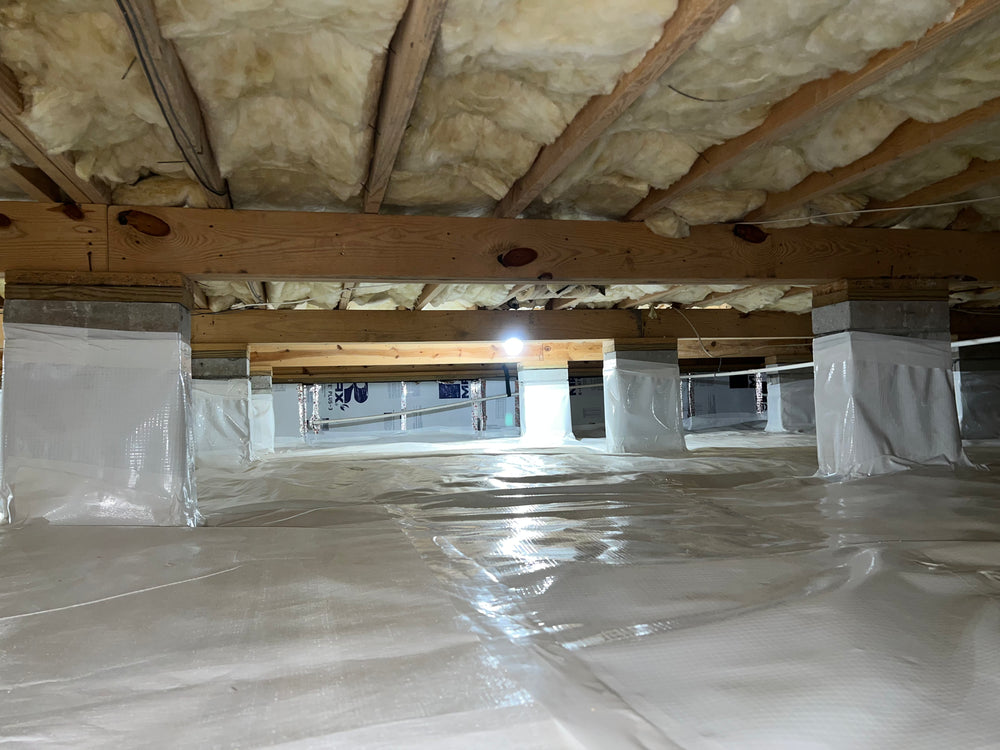 Low-angle view of a crawlspace showing vapor barrier covering the ground and concrete piers wrapped with encapsulation material