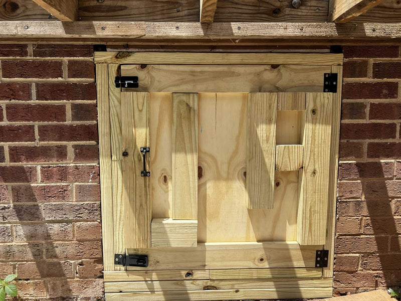 Newly built wooden crawlspace access door with black hardware mounted in a brick foundation wall