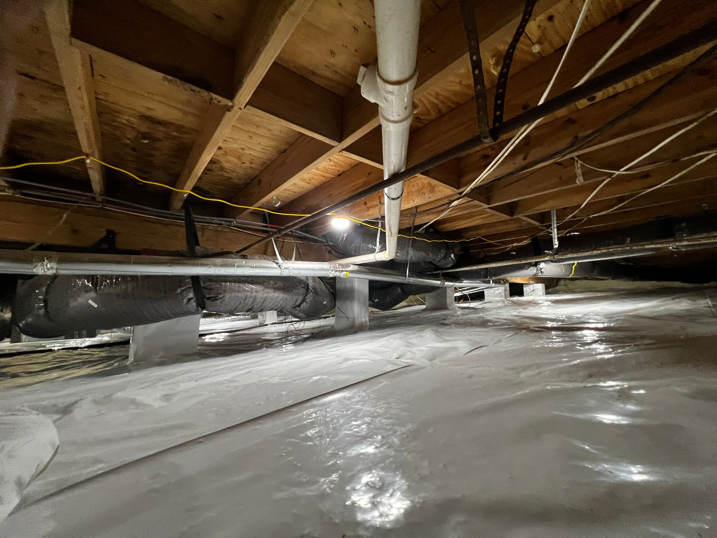 Crawlspace interior with a vapor barrier installed on the ground and exposed floor joists above