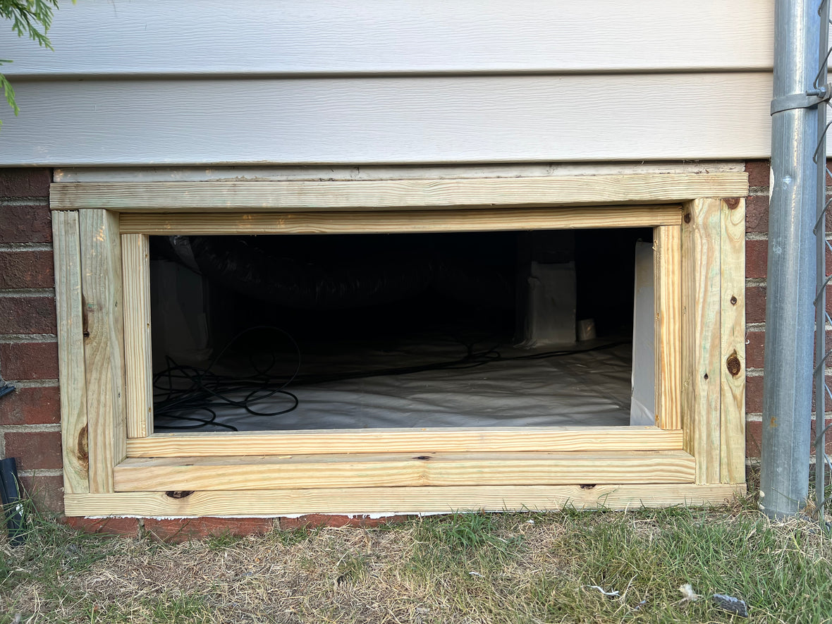 Freshly framed crawl space opening in brick foundation — pressure-treated lumber frame ready for door
