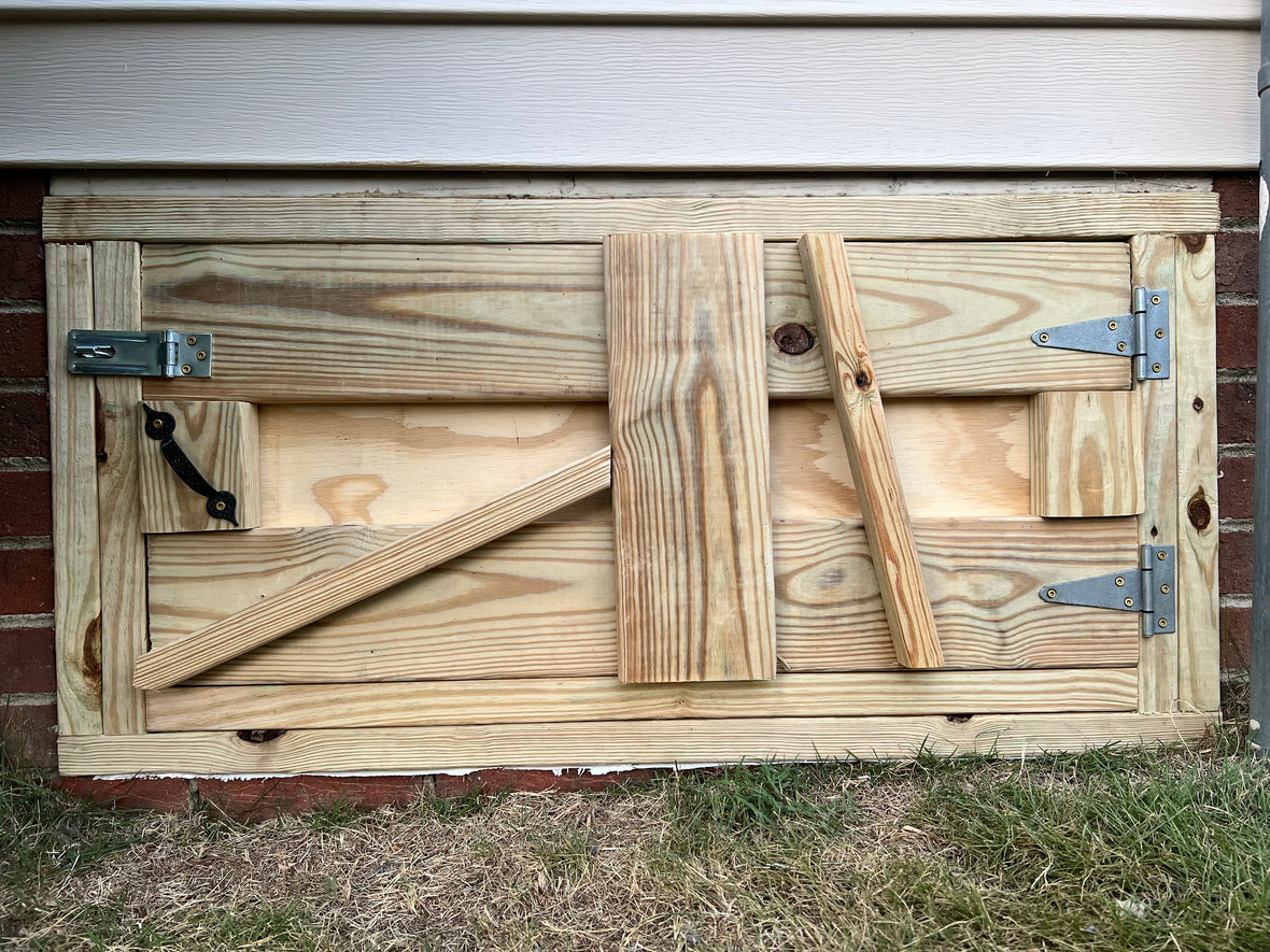 Completed custom crawl space door from rear — structural bracing, hinges, and latch hardware detail
